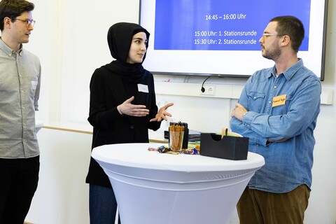 Drei Teilnehmende des Tags der Lehre stehen diskutierend um einen Bistro-Tisch.