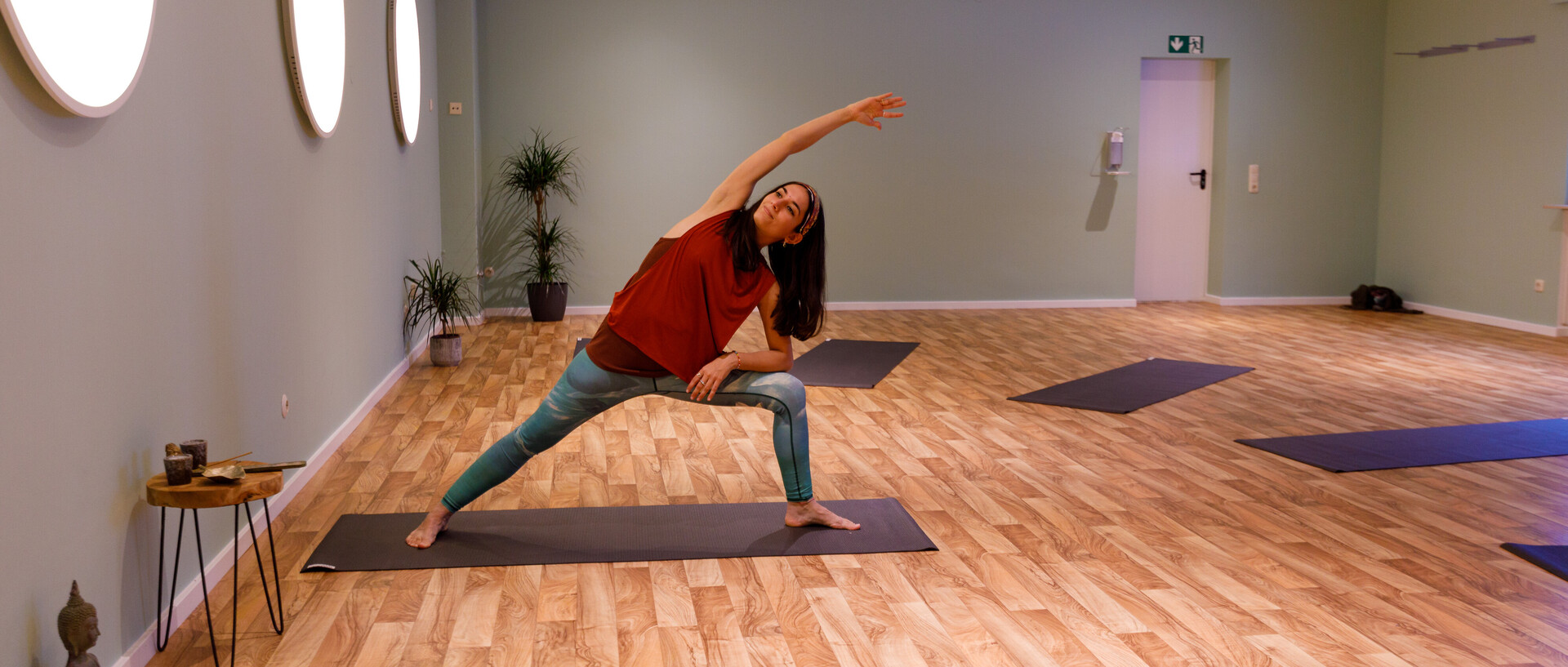 Eine weiblich gelesene Person steht auf einer Yogamatte und dehnt sich. 