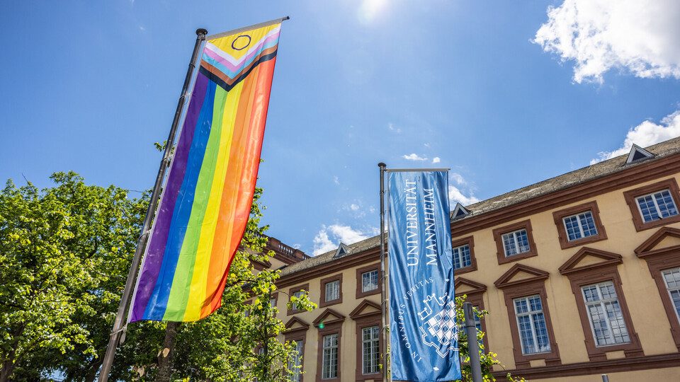 Vor dem Ostflügel des Mannheimer Schlosses wurde die Progress Pride Flag gehisst. Sie wird auch erweiterte Regenbogenflagge genannt. Daneben weht die dunkelblaue Fahne der Universität Mannheim.