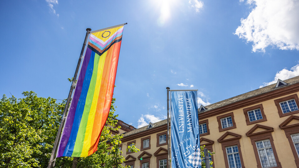 Vor dem Ostflügel des Mannheimer Schlosses wurde die Progress Pride Flag gehisst. Sie wird auch erweiterte Regenbogenflagge genannt. Daneben weht die dunkelblaue Fahne der Universität Mannheim.
