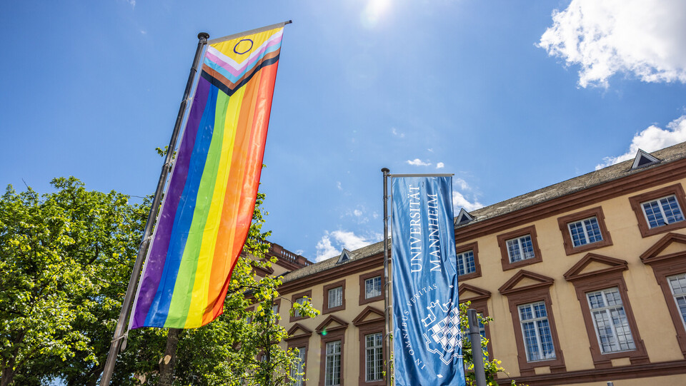 Vor dem Ostflügel des Mannheimer Schlosses wurde die Progress Pride Flag gehisst. Sie wird auch erweiterte Regenbogenflagge genannt. Daneben weht die dunkelblaue Fahne der Universität Mannheim.
