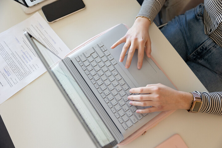 Eine Studentin arbeitet an einem Laptop. Die Aufnahme ist von oben, zu sehen sind das Gerät und die die Hände. 