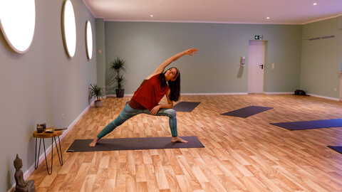 Eine Person in Sportkleidung macht Yoga auf einer Matte und befindet sich in einem leeren Yogastudio..