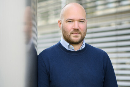 Porträt von Prof. Traunmüller. Er trägt einen dunklen Pullover und lehnt an einer Säule.