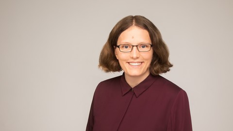 Hannah Soiné. She is wearing a red shirt in front of a grey-beige background.