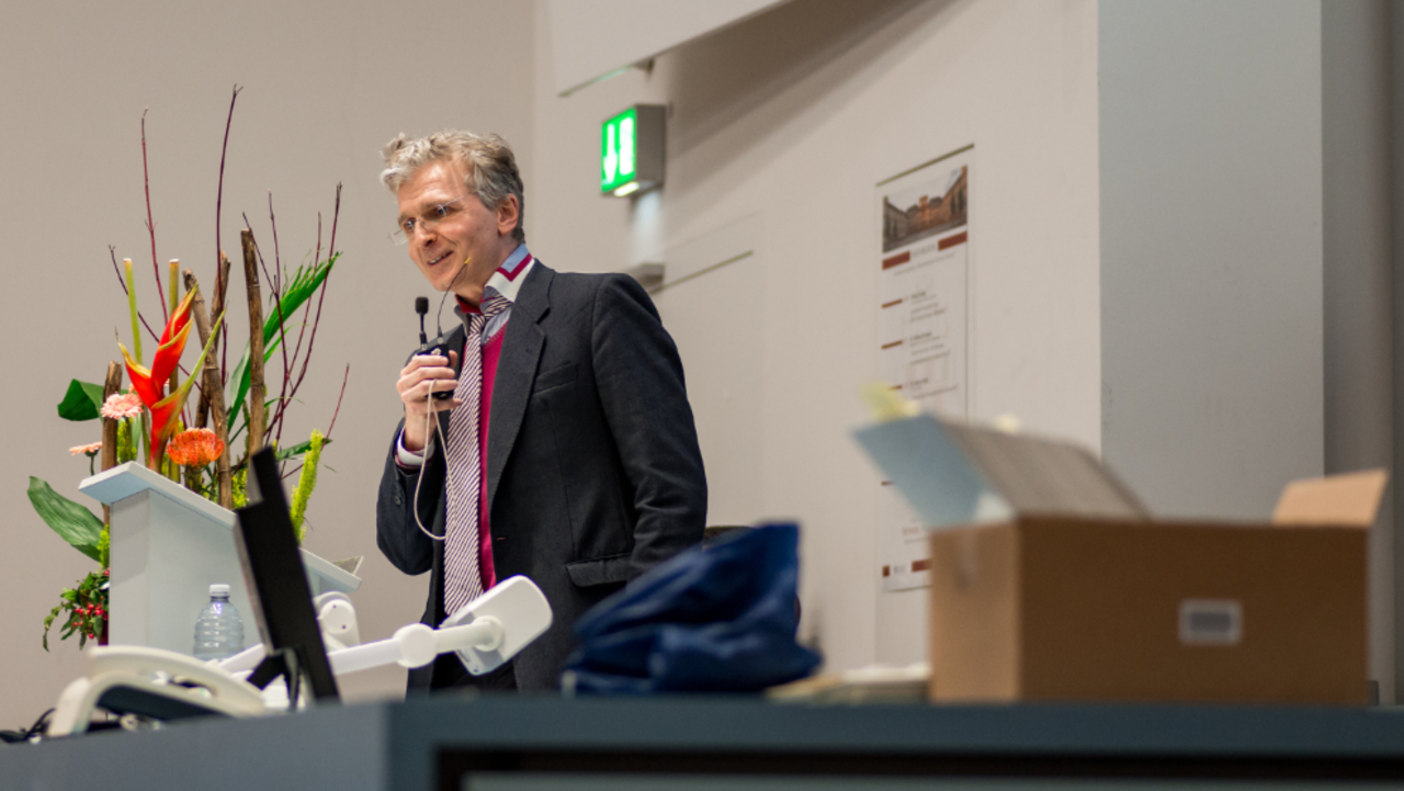 Prof. Dr. Justus Fetscher spricht in eiin Mikrophon. Neben ihm ein Blumengesteck.