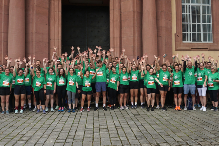 Gruppe von Läuferinnen und Läufern in grünen T-Shirts vor dem Schloss Mannheim, alle heben die Arme.