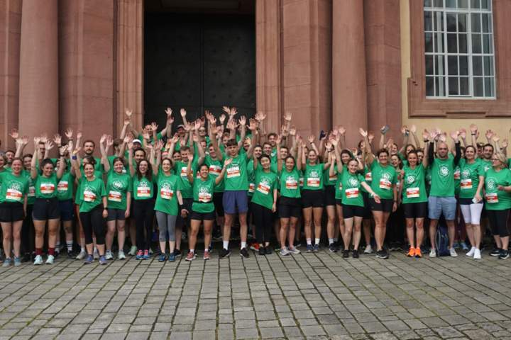 Gruppe von Läuferinnen und Läufern in grünen T-Shirts vor dem Schloss Mannheim, alle heben die Arme.