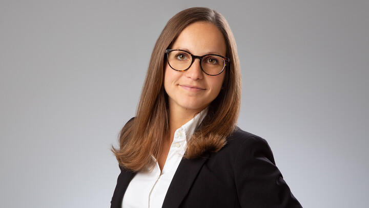 Annabelle Bröstl. She is wearing a black jacket over a white shirt and is standing in front of a grey wall.