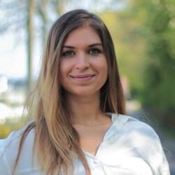 Elisabeth Schmalz hat braun-blonde, lange Haare. Sie trägt ein helles Hemd und hat ihre rechte Hand in die Hüfte gestemmt.