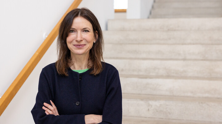 Porträtbild von Sarah Geber. Sie steht vor einer Treppe und verschränkt die Arme.
