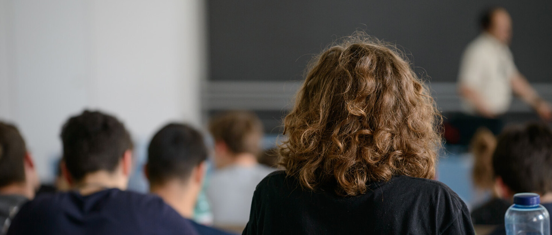 Studierende sitzen hintereinander in einem Hörsaal und hören bei einer Vorlesung zu.