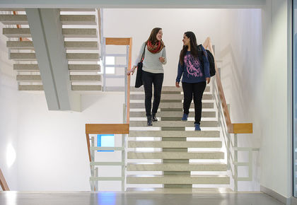 Zwei Studentinnen unterhalten sich und laufen die Treppe im Gebäude L 1 runter.