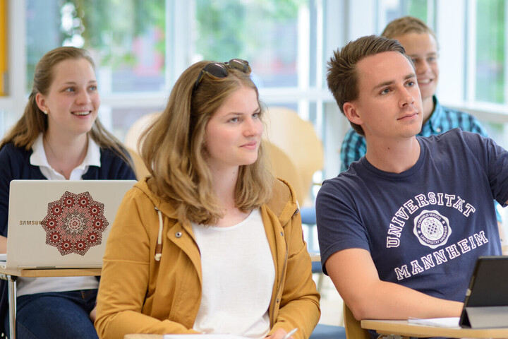 Vier Studierende sitzen in einem Seminarraum, einer meldet sich. 