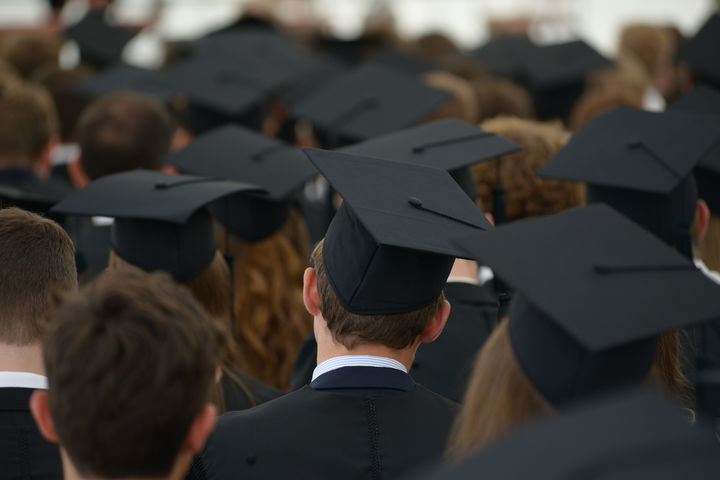 Die Hinterköpfe vieler Studenten, die bei einem Festakt einen schwarzen Absolventenhut tragen.