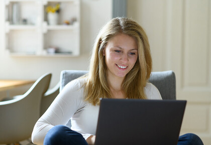 Eine Studentin sitzt am Laptop in Ihrer Wohnung. Sie sieht zurfrieden aus.