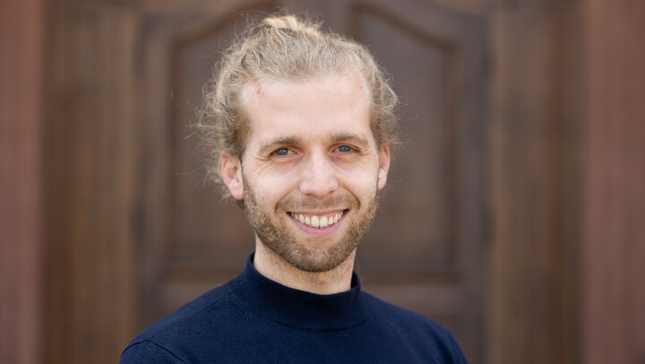 Jan Zental. He is wearing a dark blue sweater and is standing in front of brown door.
