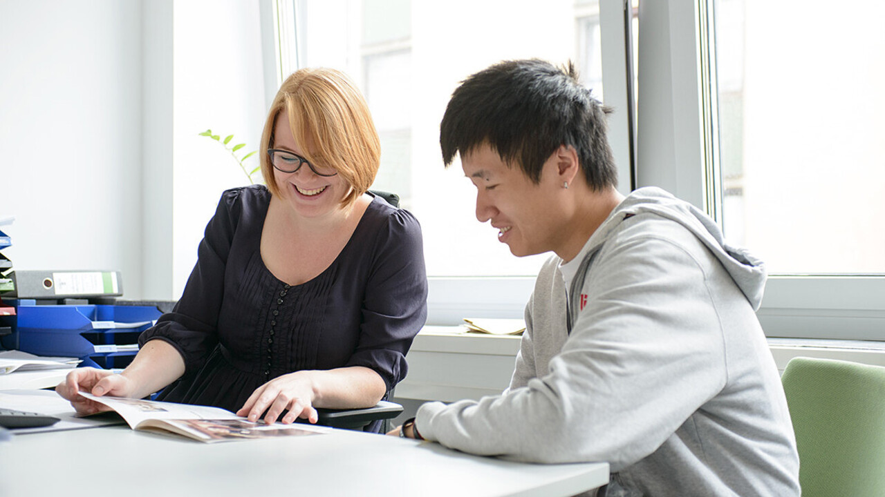 Eine lächelnde Mitarbeiterin der Universität Mannheim zeigt einem jungen Mann eine Broschüre.