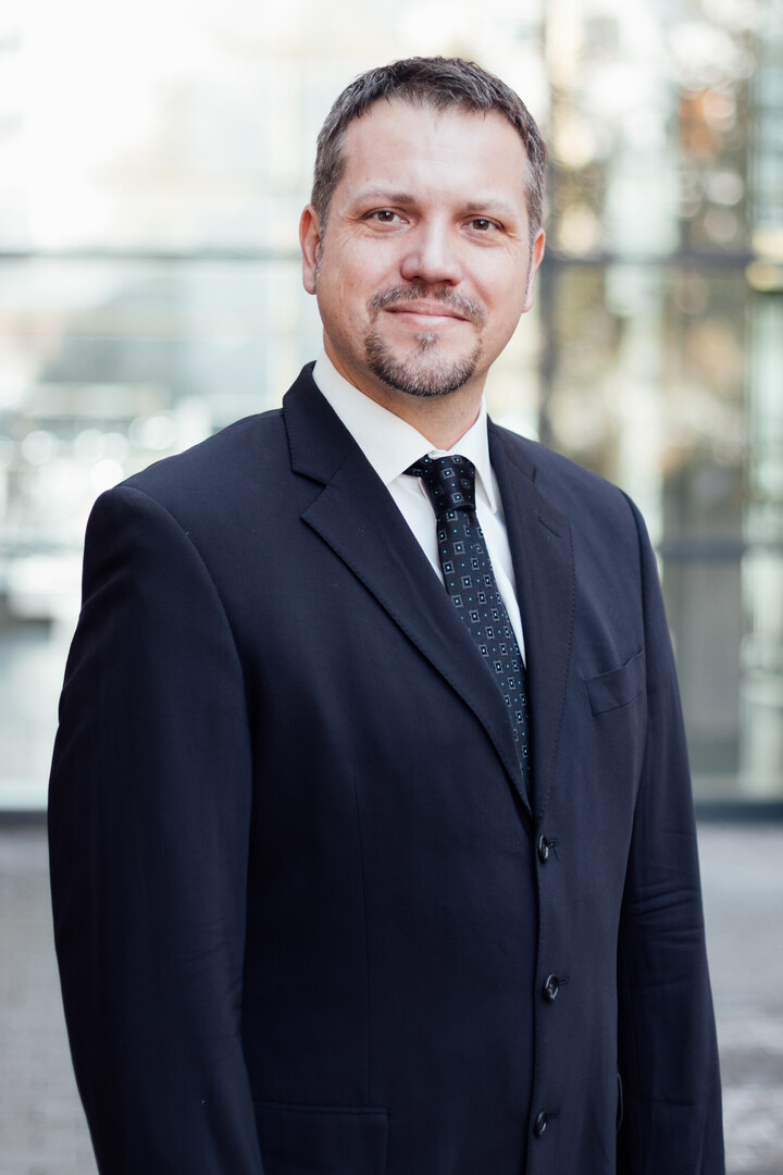 Frederik Armknecht blickt freundlich in die Kamera. Er trägt einen dunklen Anzug mit Krawatte.