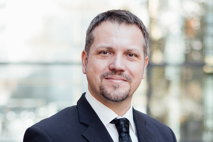Frederik Armknecht blickt freundlich in die Kamera. Er trägt einen dunklen Anzug mit Krawatte.