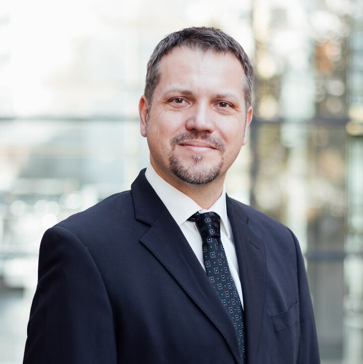 Frederik Armknecht blickt freundlich in die Kamera. Er trägt einen dunklen Anzug mit Krawatte.