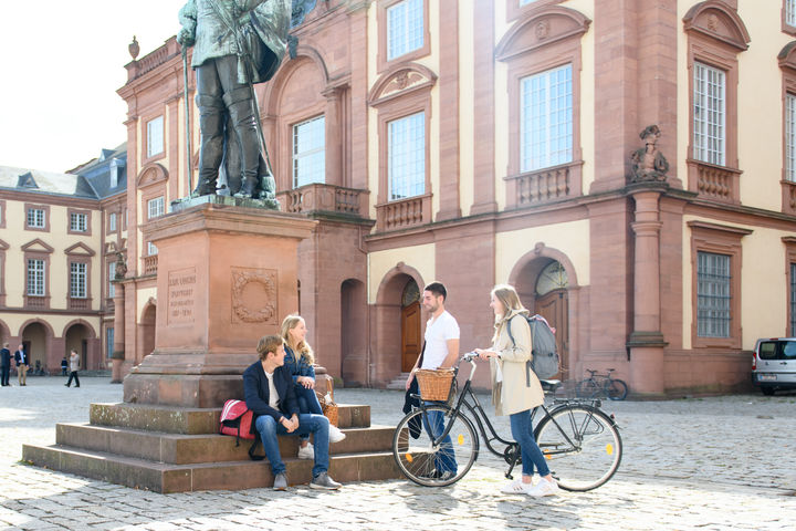 vier Studierende sitzen auf dem Ehrenhof der Universität Mannheim.