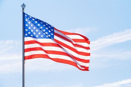 Amerikanische Flagge weht im Wind. Im Hintergrund ein blauer Himmel mit Wolkenstreifen.