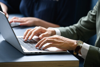 Zwei Personen sitzen am Tisch und tippen auf ihre Laptops.