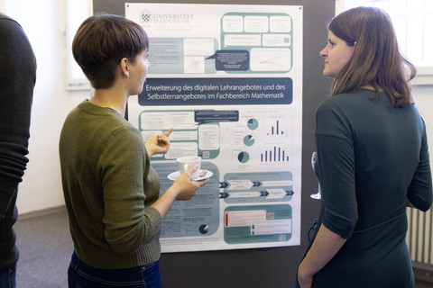 Zwei Frauen stehen vor einer Poster-Stellwand und unterhalten sich. Das Poster hat den Titel "Erweiterung des digitalen Lehrangebots und des Selbstlernangebotes im Fachbereich Mathematik".  