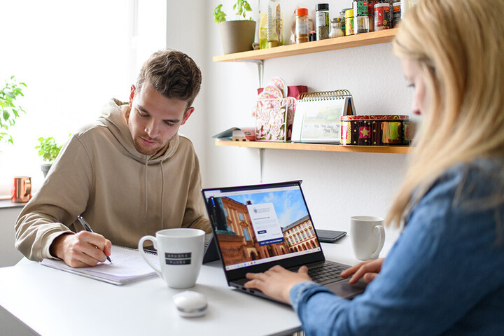 Eine junge Frau und ein junger Mann arbeiten gemeinsam in der Küche am Tisch.