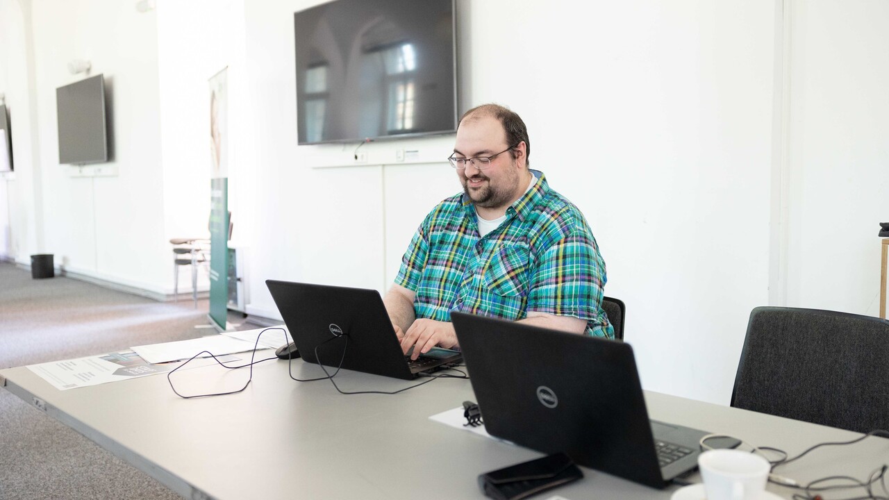 Mitarbeiter der Uni Mannheim sitzt mit Laptop an einem Infotisch