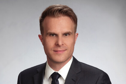 Portraitfoto von Prof. Dr. Florian Stahl vor einem grauen Hintergrund. Er trägt ein weißes Hemd, eine schwarze Krawatte und ein schwarzes Sakko.