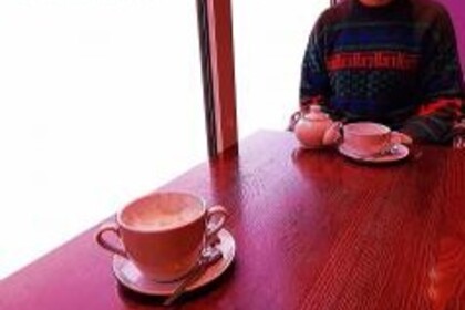 Eine Person sitzt hinter einer Teetasse, gegenüber steht eine Kaffeetasse.