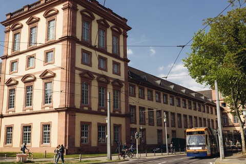 Der Eckturm am Ostflügel des fensterreichen Mannheimer Schlosses. Auf der Straße fahren eine Straßenbahn und Radfahrer.
