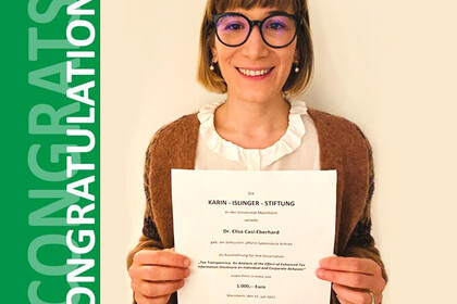 Elisa Casi-Eberhard. She is wearing a brown jacket over a white shirt and is holding a paper in front of a yellowish background.