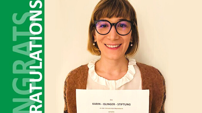 Elisa Casi-Eberhard. She is wearing a brown jacket over a white shirt and is holding a paper in front of a yellowish background.