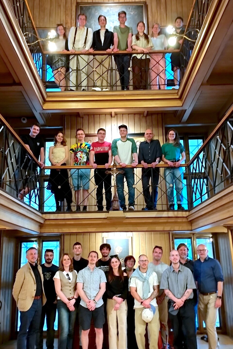 Ein Gruppenfoto der Teilnehmender der Summer School, die in einem holzgetäfelten Raum mit zwei Balkonen stehen.