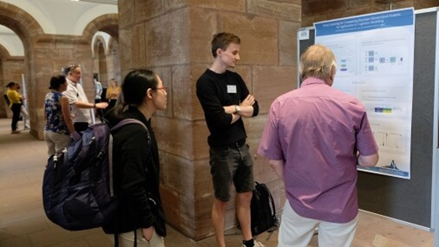 Picture showing a PhD Candidate in front of his poster with some visitors