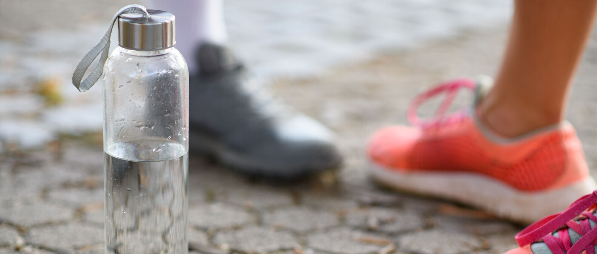 Eine Trinkflasche mit Wasser, daneben Blick auf die Laufschuhe von zwei Personen.