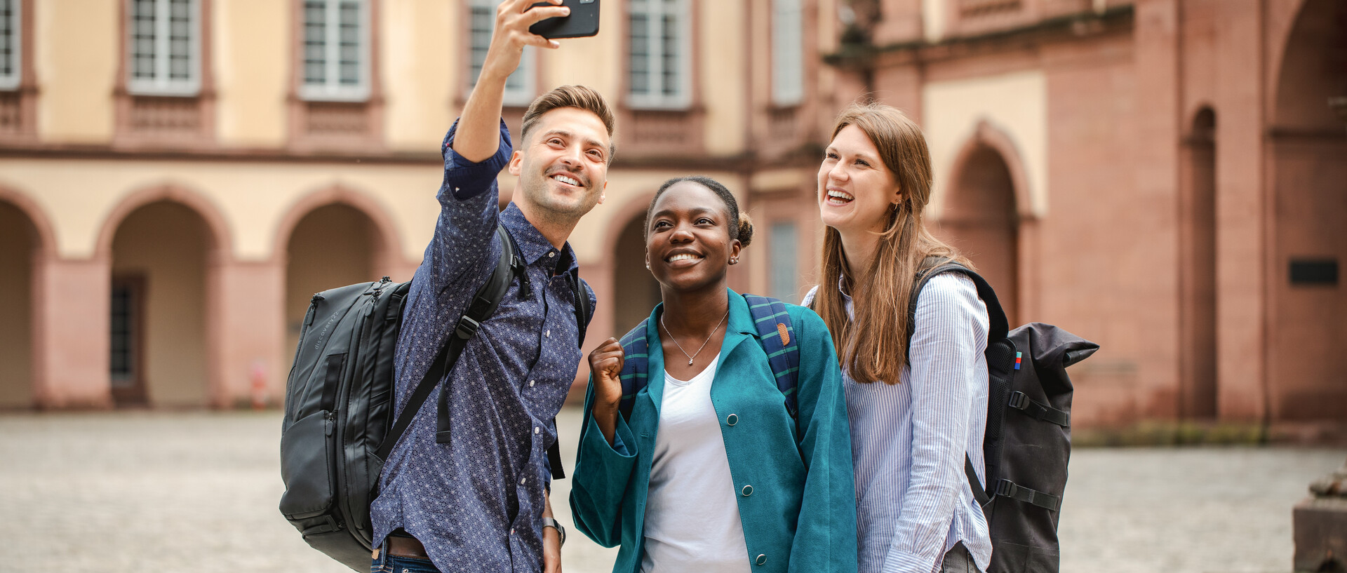 Two women and a man standing together in front of the Mannheimer castle.