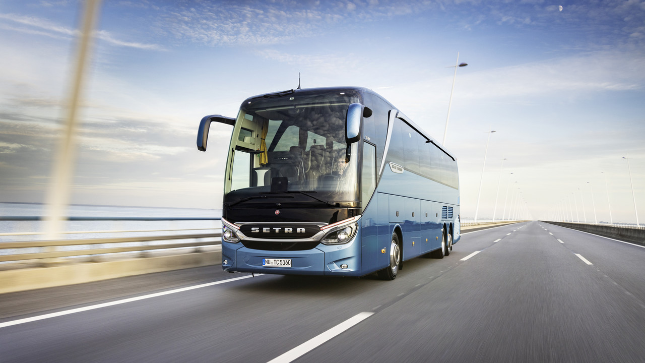 Ein blauer Reisebus fährt über eine Brücke. Im Hintergrund das Meer.