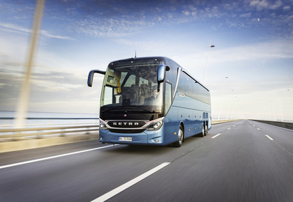 Ein blauer Reisebus fährt über eine Brücke. Im Hintergrund das Meer.