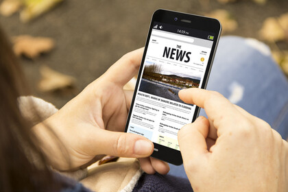 Eine Person hält ein Smartphone in der Hand. Auf dem Bildschirm ist das Wort "News" lesbar.