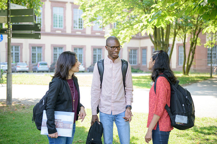 Drei Studierende mit Rucksäcken im Gespräch auf dem Campus der Universität Mannheim.