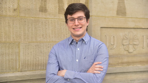 Carlos Gueiros. He is wearing a blue shirt and is standing in front of a brown house wall.