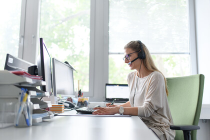 Mitarbeiterin sitzt mit Headset vorm Computer.