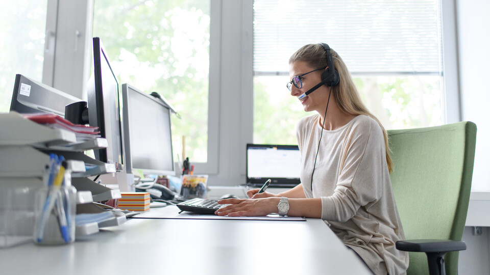 Koordinationsstelle für Studieninformationen Mitarbeiterin sitzt mit Headset vorm Computer.