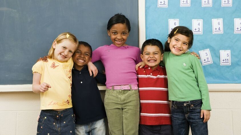 Vier Kinder mit bunten T-Shirt stehen lachend in einer Reihe und haben sich im Arm.
