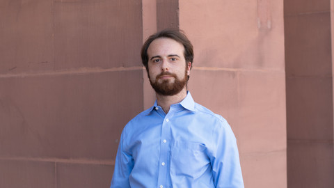 Jacopo Gambato. He is wearing a blue shirt and is standing in front of a brown stonewall.