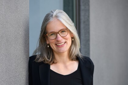 Gesundheitspsychologin Prof. Dr. Jutta Mata lehnt an eine Betonwand und lächelt. Sie trägt einen schwarzen Blazer und ein schwarzes T-Shirt.
